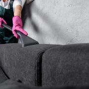 cropped shot of woman in rubber gloves cleaning sofa with vacuum cleaner