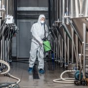 Factory cleaning. Man in protective suit and mask disinfects plant